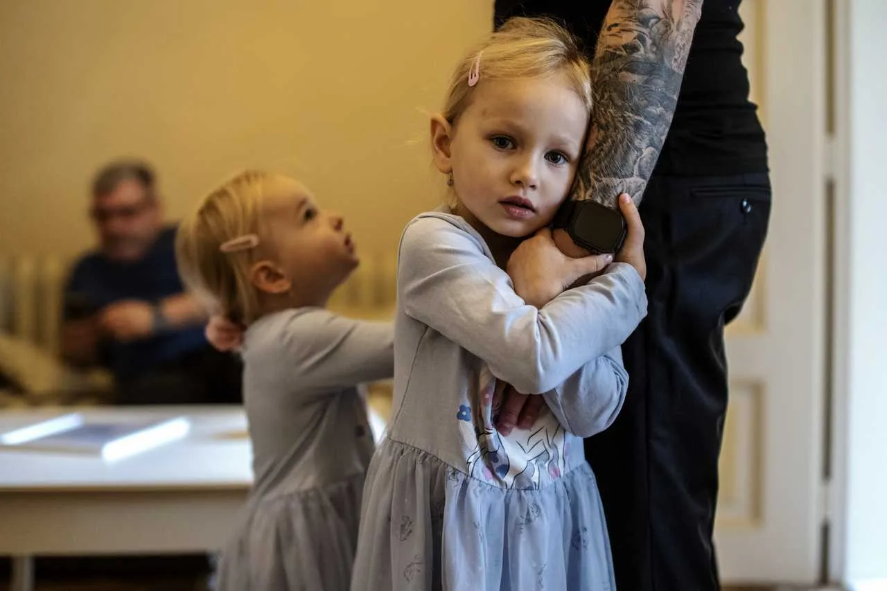 Dcérka drží otca za ruku a pozerá do kamery